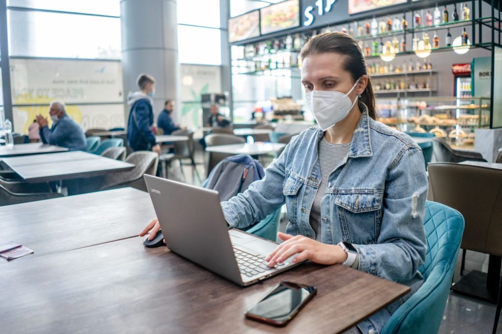 A woman wearing a face mask works on her laptop at a café amidst a pandemic.