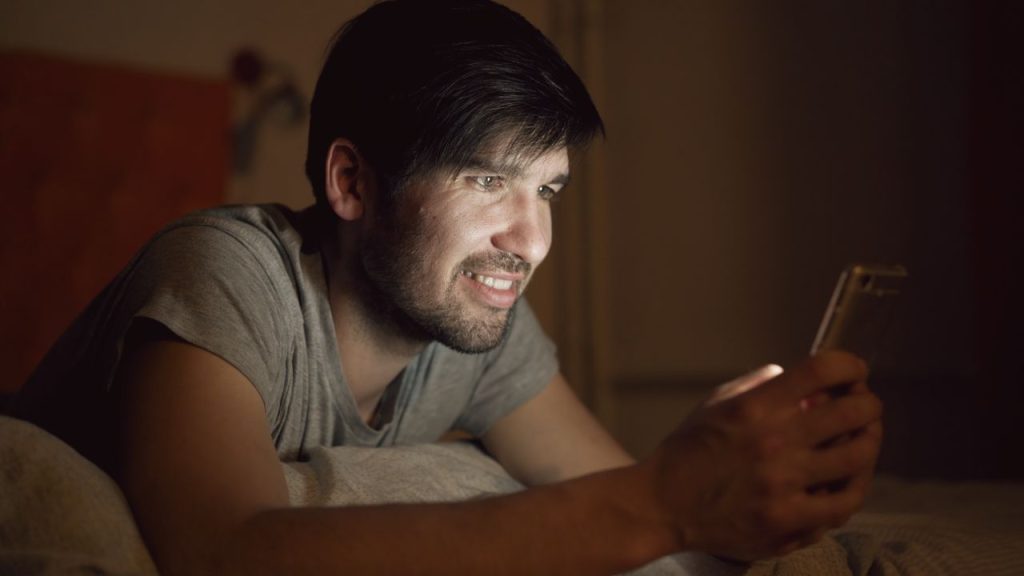 A man enjoys a late-night phone screen, illuminating his face.